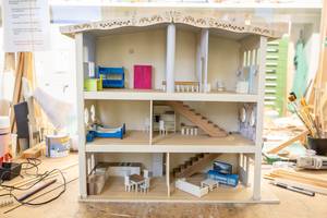 Zu sehen ist ein Puppenhaus aus Holz mit kleinen Möbeln. 