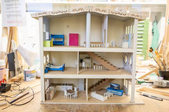 Zu sehen ist ein Puppenhaus aus Holz mit kleinen Möbeln. 