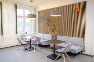 Zu sehen ist die neue SRH Lounge mit einem Sofa und einer Holzwand. 